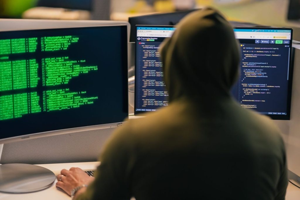 person looking at dual monitors with complex code and neural network diagram