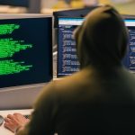 person looking at dual monitors with complex code and neural network diagram